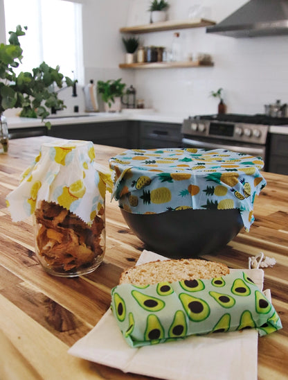 Kitchen with a jar, bowl, and sandwich wrapped in wax wraps on a butcher block.