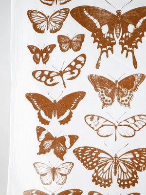 Close up of a white tea towel that has a variety of terra cotta colored butterflies.