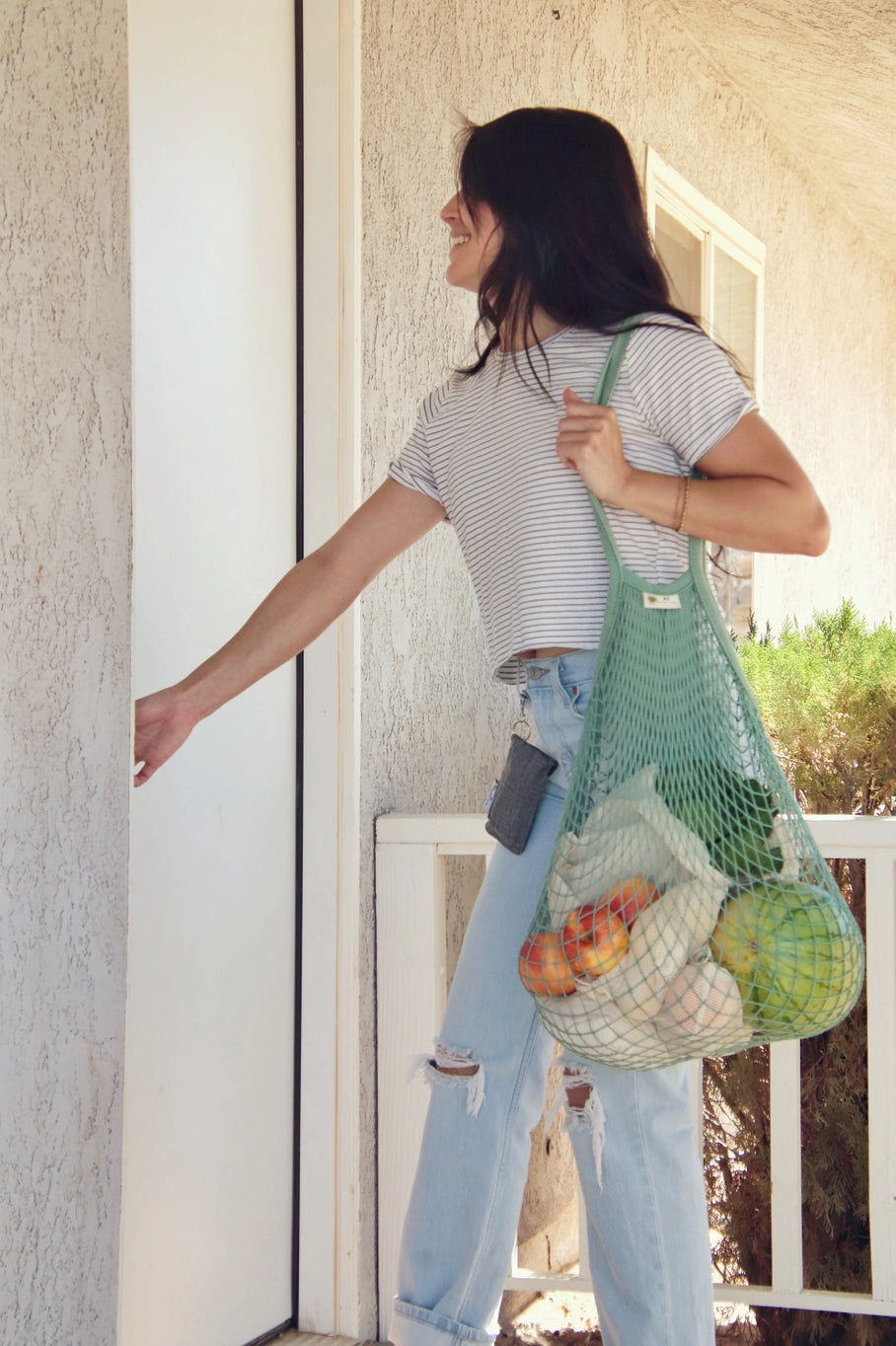 Women carrying sage green mesh bag carrying produce.