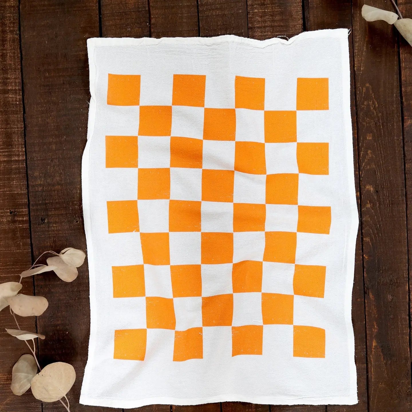 wooden background, white tea towel with orange checkers.