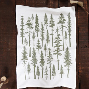 Wooden background with a white tea towel that has green redwood trees.