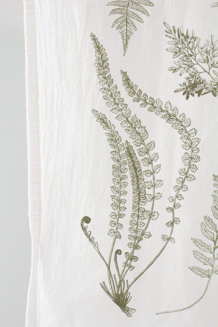 Close up of a white tea towel with fern fronds.