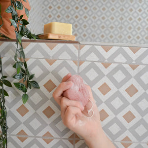 Patterned tile background with a hand holding a pink Konjac sponge.