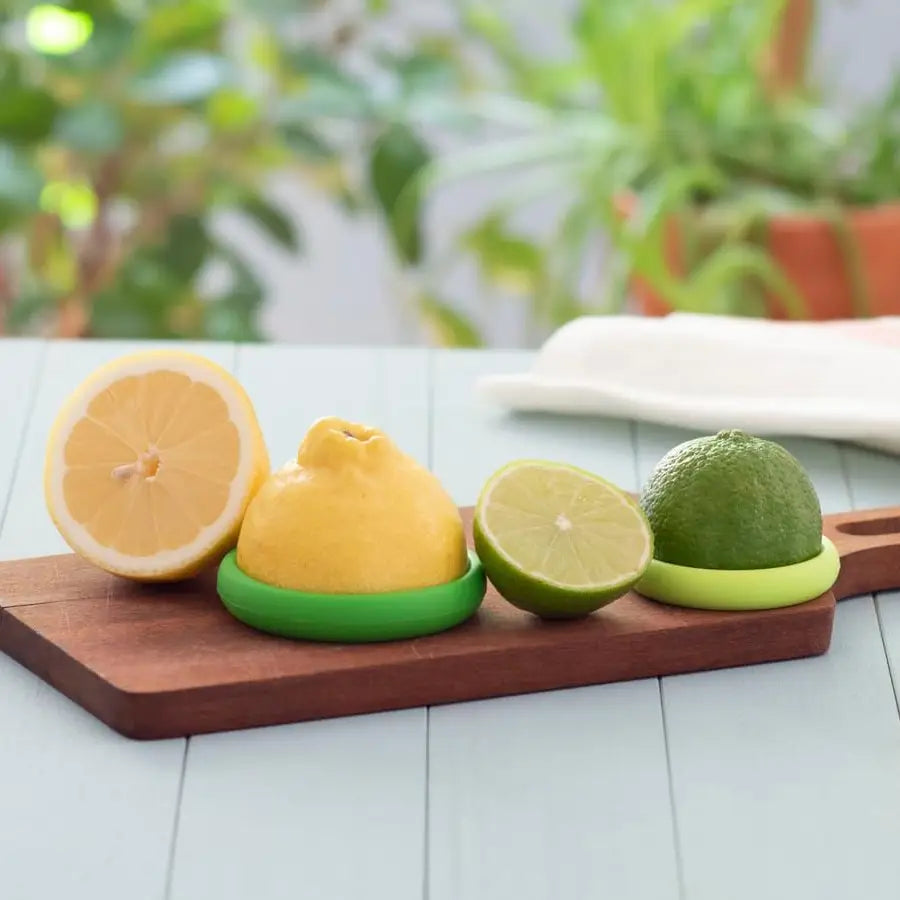 A lemon & lime with food huggers on a wooden cutting board.