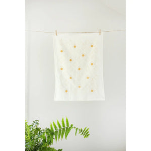 Green ferns with a white tea towel that has a yellow sunburst pattern.