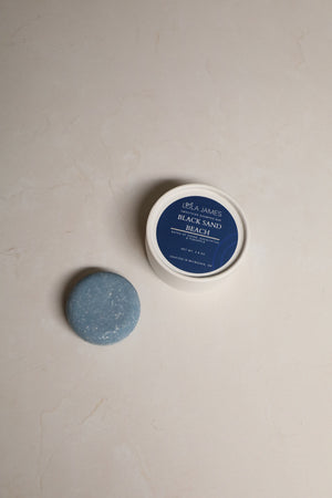 Round, blue shampoo bar sitting next to packaging.