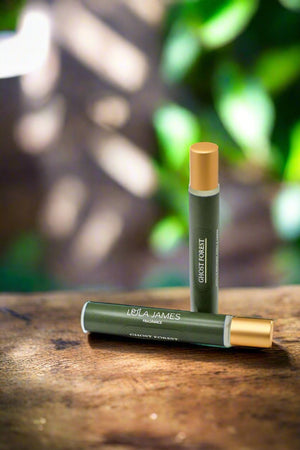 Green rollerball with gold lid on wooden table, leaves in background.