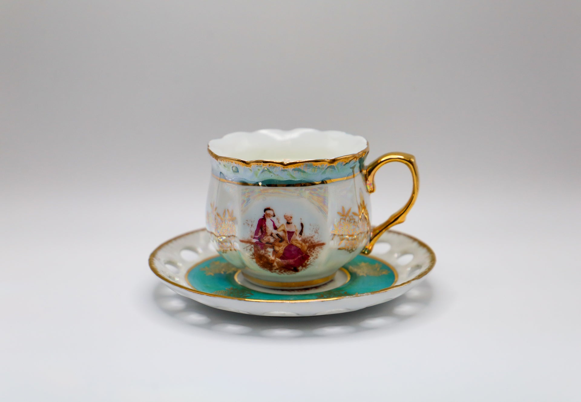 Petit cup and saucer in soft teal blue with gold accents and rich ruby jewel tone detail in the colonial couple on the side of the cup.  Leafy green floral and citrus scent.