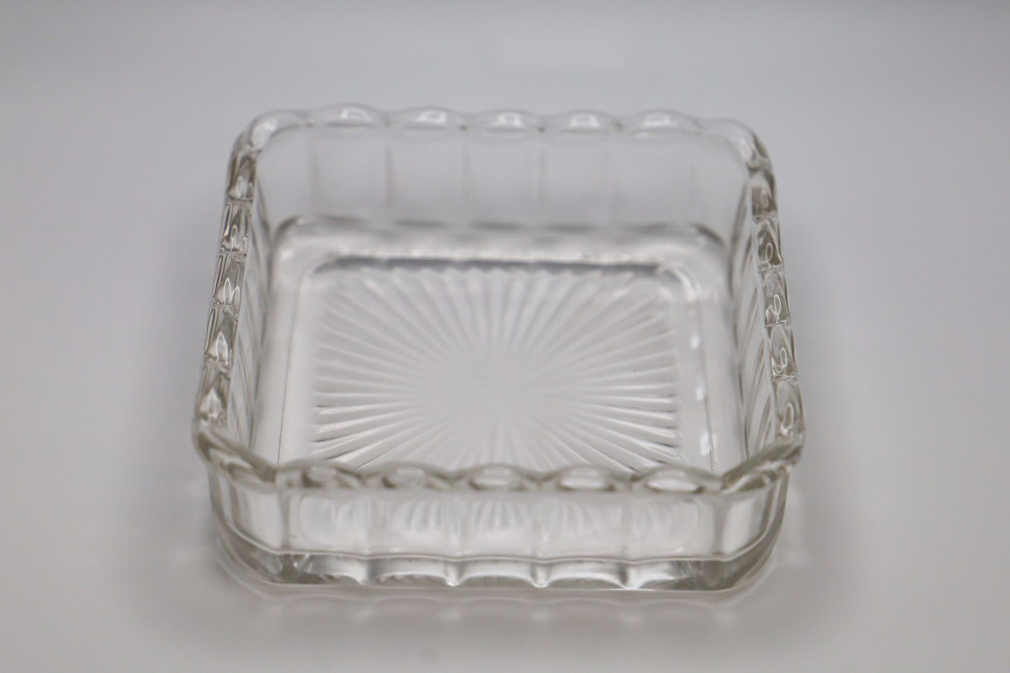 Clear glass bowl in unusual square shape, with scalloped top, ribbed sides, and starburst pattern on the bottom.