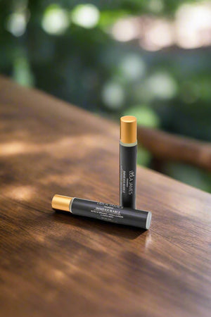 Black rollerball with gold lid, laying on wooden table with green leaves in background.