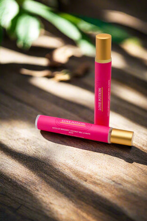 Pink rollerball with gold lid, laying on wooden table with leaves in the background.