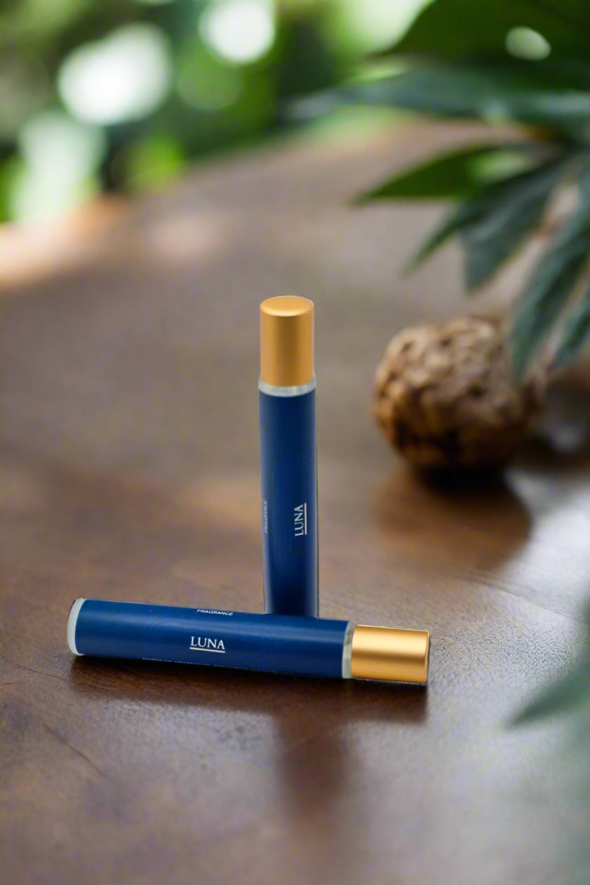 Blue rollerball with gold laying on wooden table, green leaves in background.