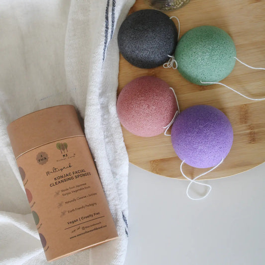 4 Konjac sponges laying on a bamboo tray. Cardboard packaging laying nearby on a towel.