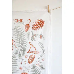 Close up of a white tea towel with fern fronds, mushrooms, and pine cones.