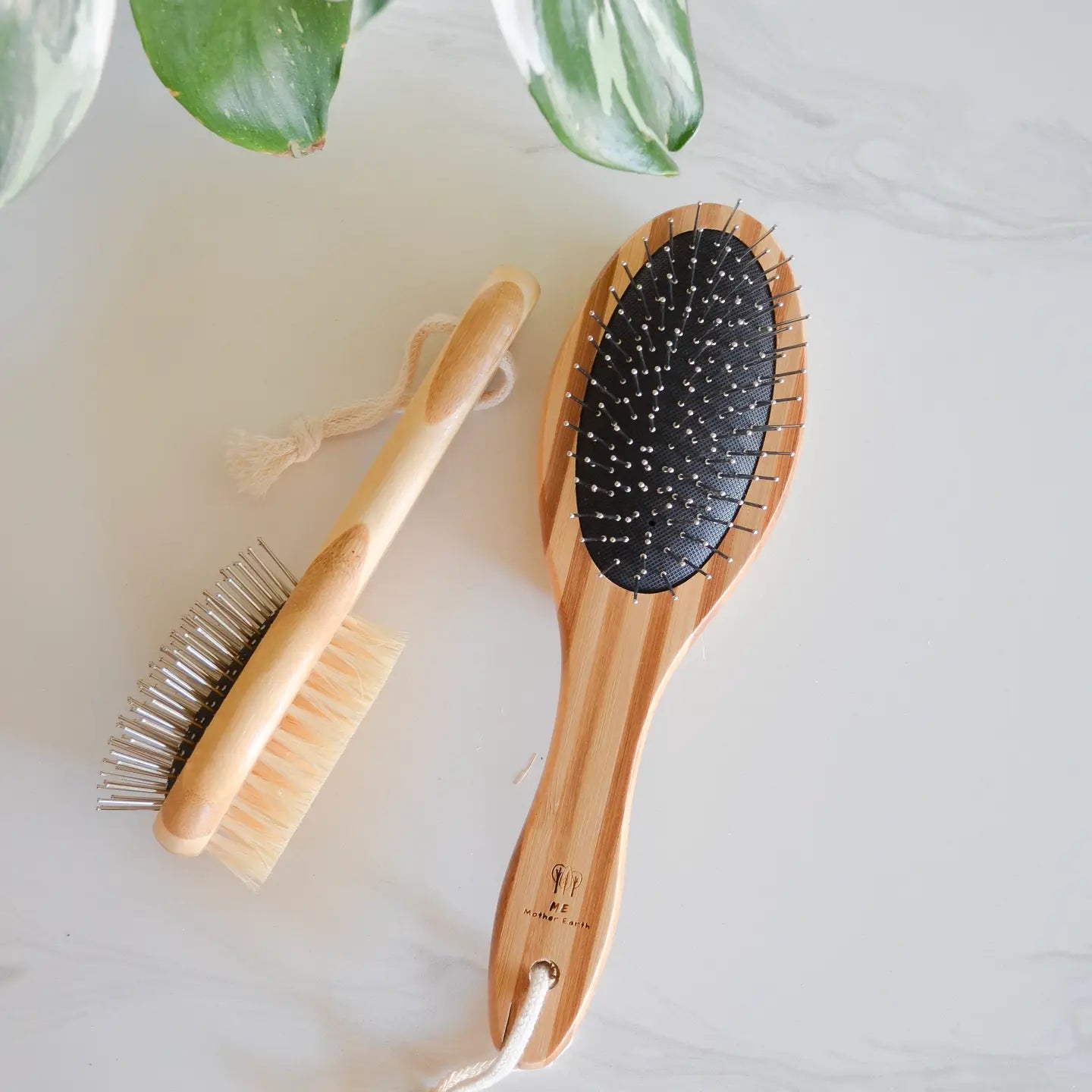 A small bamboo pet brush laying on its side with a bristle and metal pin side. Large pet brush laying next to it.