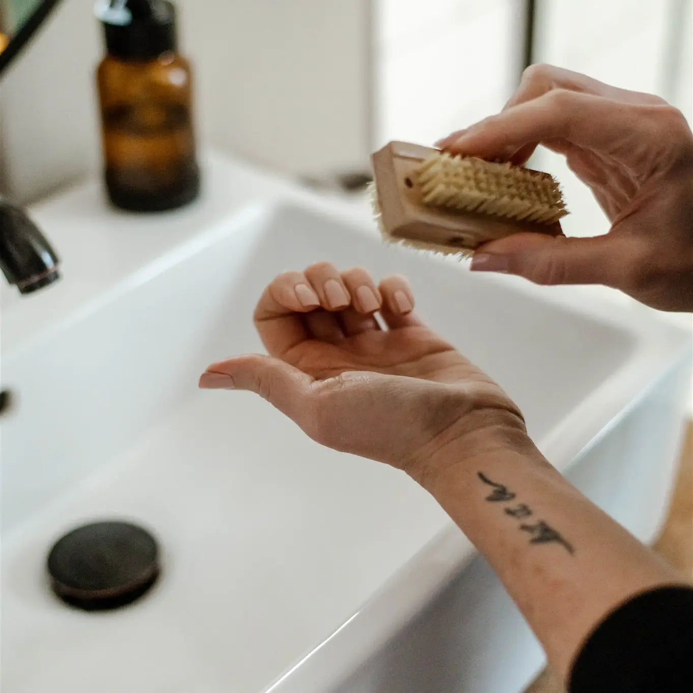 Woman holding a nail brush up to her fingers, sink in the background.