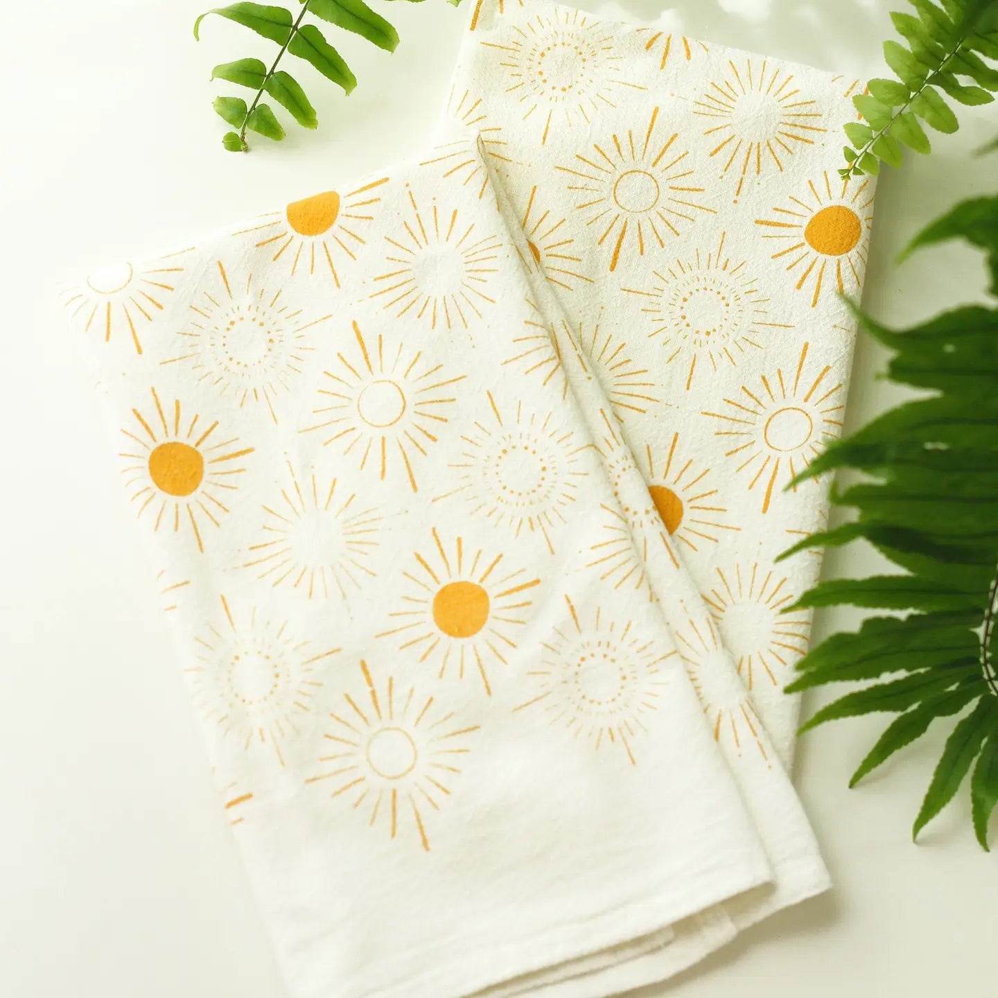 Green fern fronds with a stack of tea towels that have a yellow diamond stardust pattern.