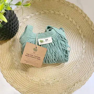 Tan circular place mat with sage green mesh bag folded. 