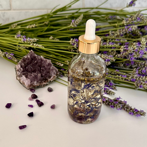 A bottle of oils infused with botanicals and amethyst crystals with amethyst and lavender nearby.